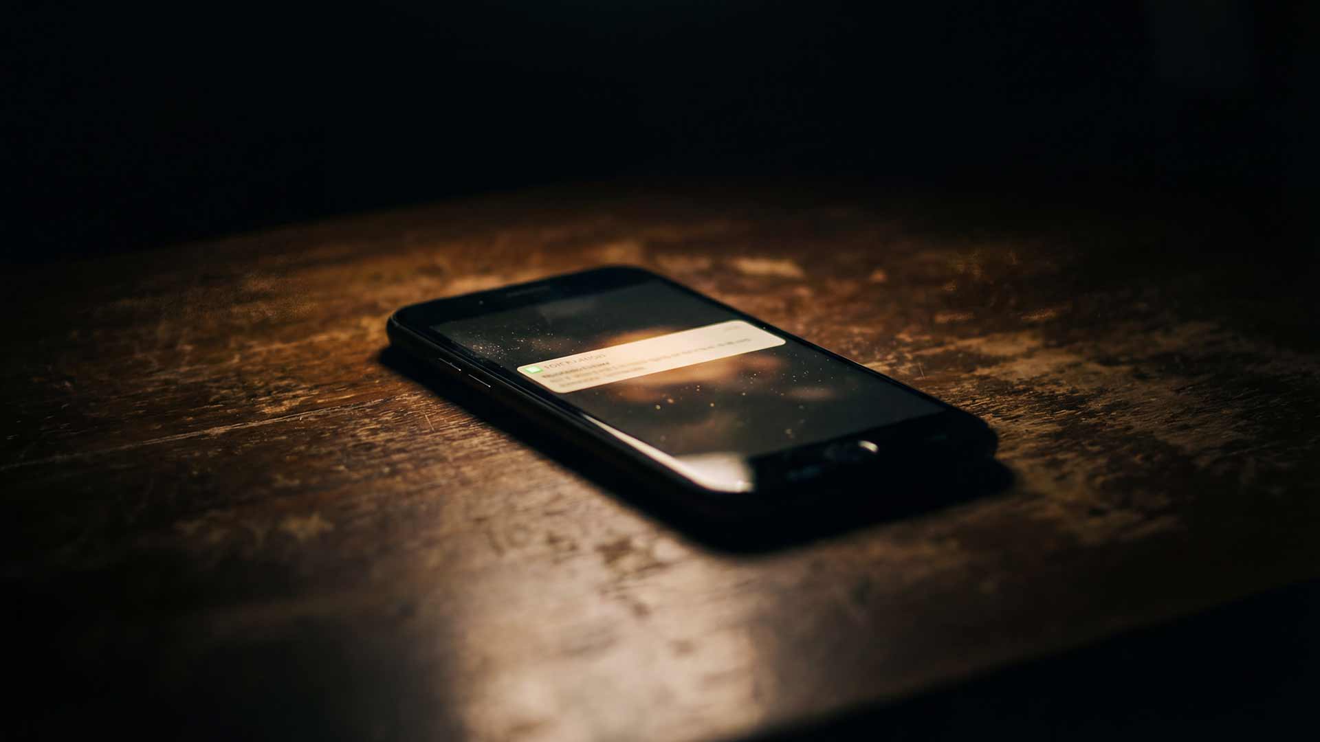 Phone notification glowing on dark wooden table
