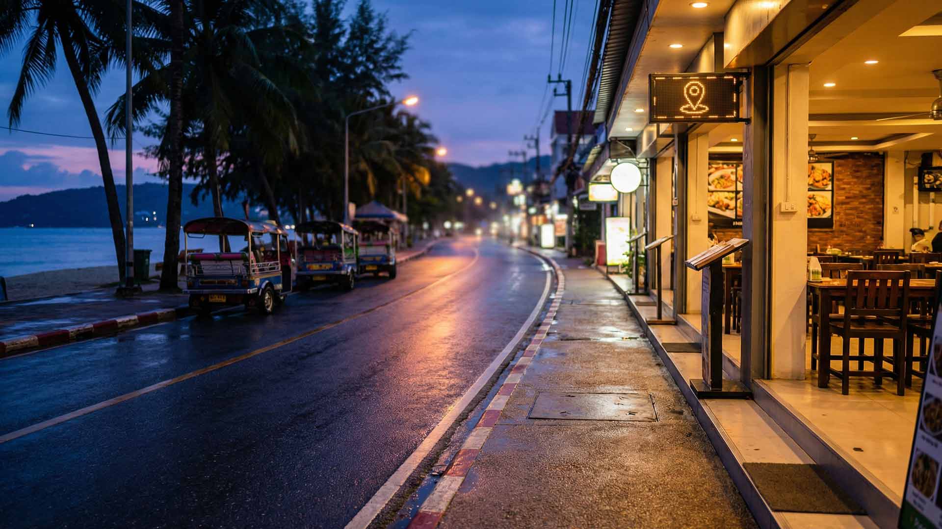 Rain-slicked Patong beachfront road at dusk with a neon Google Maps pin sign glowing above a restaurant, colourful tuk-tuks parked along palm-lined shoreline
